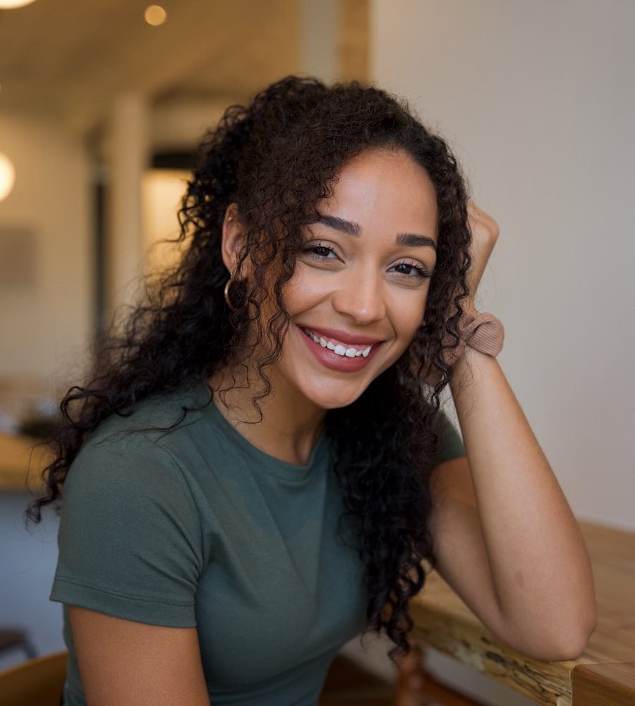 Mulher sorrindo, apoiada em uma mesa